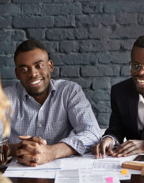 Unrecognizable female with shirt hairstyle is about to be hired for desired position in large company by two cheerful dark-skinned handsome recruiting experts, laughing happily during job interview